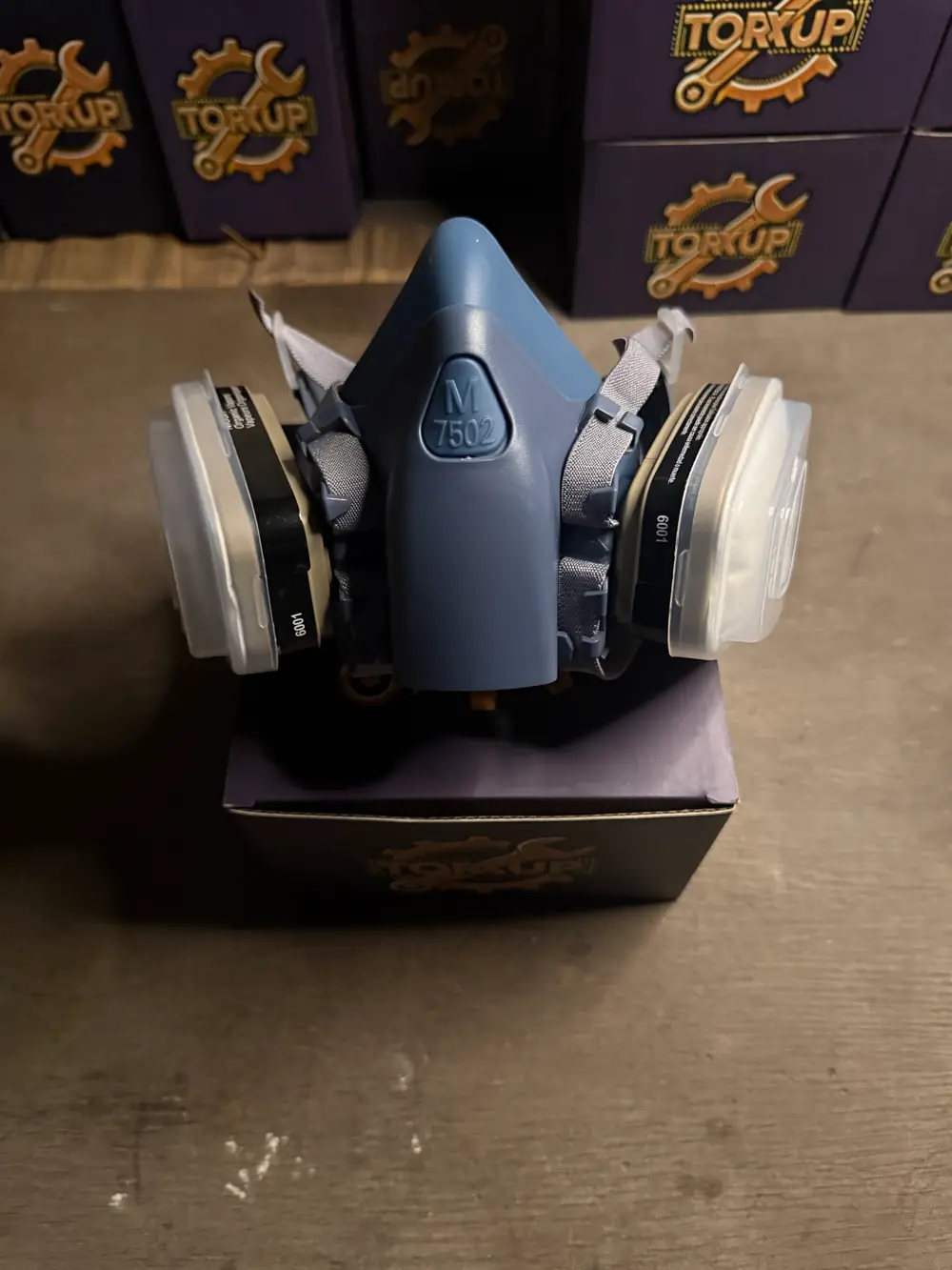 Torxup CoreMask respirator front-on, sitting on its box in the workshop, Torxup boxes stacked behind.